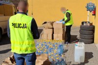Policjanci weryfikują z dokumentacją przygotowywany do transportu alkohol znajdujący się w butelkach z tworzywa sztucznego. Część butelek umieszczona jest w kartonach.