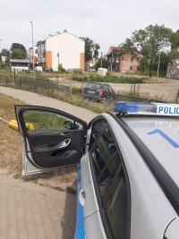 policyjny radiowóz a w tle rozbite w wyniku zdarzenia auto ososbowe
