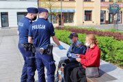 policjanci rozdają mieszkańcom Tomaszowa maseczki ochronne. Na ławce siedzi kobieta i mężczyzna
