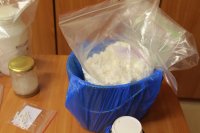 zabezpieczone przez policjantów narkotyki biały proszek w plastykowym wiadrze i w foliowej torbie, pojemniki z cieczą torebka foliowa z białymi tabletkami