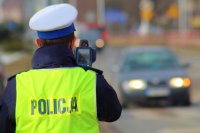 umundurowania policjanci ruchu drogowego w kamizelkach odblaskowych i czapkach z białym otokiem w trakcie pracy z urządzeniem - pomiaru przy drodze po której poruszają się pojazdy