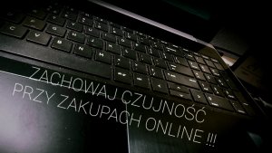 zdjęcie w ciemnych kolorach, widoczna klawiatura komputerowa i skośny napis o treści zachowaj czujność przy zakupach online
