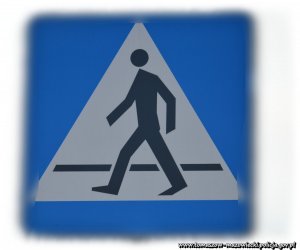 biało- niebieski znak drogowy na rozmytym tle - przejście dla pieszych