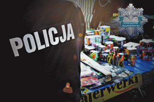 plecy policjanta w umundurowaniu z napisem POLICJA na tle straganu z fajerwerkami
