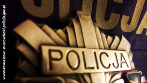 policyjna odznaka z napisem policja położona na mundurze na którym częściowo widać napis policja