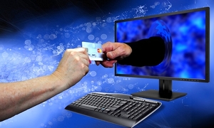 dłoń trzymająca kartę kredytową i wyciągnięta druga dłoń wychodząca z ekranu komputera sięgająca po tę kartę