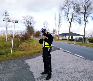 policjant ruchu drogowego dokonuje laserowym miernikiem pomiaru prędkości