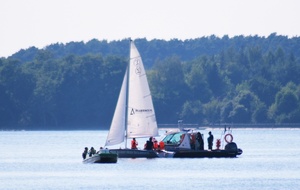 policyjna łódź motorowa na wodzie podpływa do żaglówki na której znajdują się uczestnicy obozu letniego