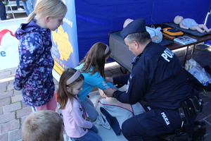 Funkcjonariusz  Policji prezentujący zgromadzonym dzieciom udzielanie pierwszej pomocy.