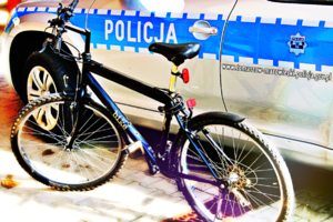zdjęcie poglądowe roweru w kolorze czarnym w tle widoczny radiowóz policyjny