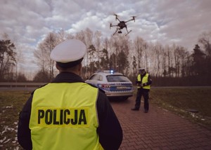 dwaj umundurowani policjanci , dron i radiowóz