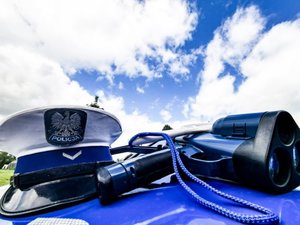 policyjna czapka ruchu drogowego i radar laserowy na masce radiowozu. w tle błękitne niebo i białe obłoki