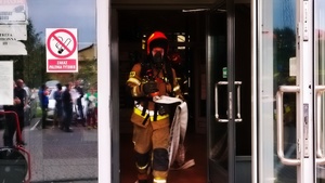 działania ewakuacyjne i gaśnicze - symulacja . ludzie zgromadzeni przed budynkiem strażacy i wozy strażackie