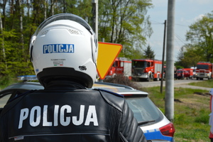 policjant na motocyklu. na tyle kasku i kurtki napis policja . w tle służby ratunkowe