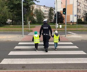 Policjant prowadzi dzieci przez przejście dla pieszych
