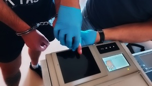 technik kryminalistyki pobiera odciski palców od zatrzymanej osoby. mężczyzna na nadgarstkach dłoni ma nałożone kajdanki