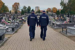 Umundurowani policjanci idą cmentarną alejką