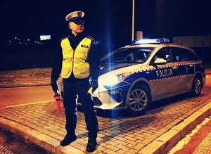 policjant ruchu drogowego stoi przed radiowozem z urządzeniem do pomiaru zawartości alkoholu w wydychanym powietrzu
