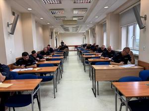 sala na której przy ławkach siedzą umundurowani policjanci rozwiązujący pisemny test