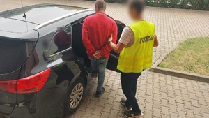 policjant prowadzi zatrzymanego mężczyznę do pojazdu