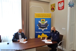 Komendant Powiatowy Policji w Tomaszowie Mazowieckim i Wójt Gminy Tomaszów siedzą przy stole konferencyjnym i podpisują umowę w sprawie służb ponadnormatywnych