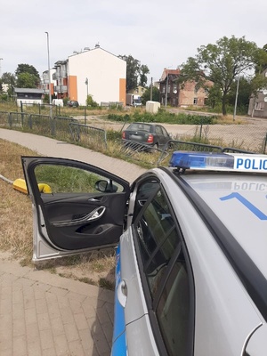 policyjny radiowóz a w tle rozbite w wyniku zdarzenia auto ososbowe