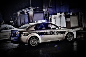 policyjny radiowóz zabezpieczający zdarzenie drogowe. W tle widoczne wozy bojowe straży pożarnej