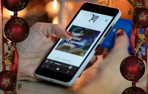 lewa dłoń kobieca ze smartfonem. obok świąteczne bombki