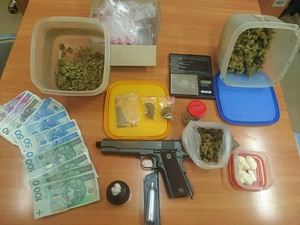 zdjęcie zabezpieczonych narkotyków. Widoczne plastykowe pojemniki otwarte z  suszem roślinnym, bały proszek, pieniądze oraz pistolet