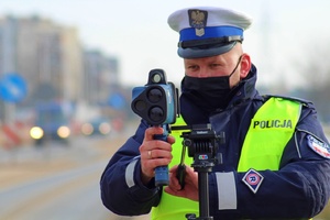 umundurowania policjanci ruchu drogowego w kamizelkach odblaskowych i czapkach z białym otokiem w trakcie pracy z urządzeniem - pomiaru przy drodze po której poruszają się pojazdy