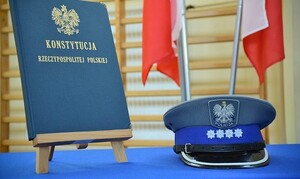 na niebieskim materiale w stojaku stoi Konstytucja a obok po prawej stronie oficerska czapka policyjna