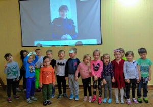 grupa przedszkolaków stoi pod ekranem na którym widać tomaszowską policjantkę wyświetlaną z rzutnika podczas połączenia online