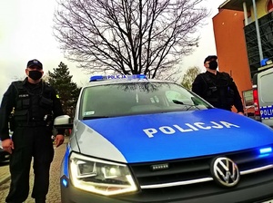 umundurowani policjanci stoją przy oznakowanym radiowozie z włączonymi sygnałami świetlnymi