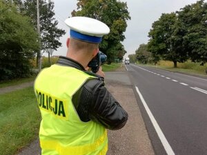 policjant w białej czapce mierzy prędkość stojąc przy ulicy