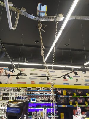 na zdjęciu widoczne wnętrze sklepu z elektroniką rozstawioną na regałach. W centralnej części u góry widoczna dziura w suficie oraz wiązką przewodów elektrycznych związana w pęk i opuszczona do dołu.