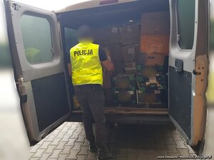 policjant w odblaskowej kamizelce z napisem policja z części ładunkowej auta dostawczego wyjmuje kartony z zabezpieczonym podczas przeszukań towarem