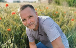 uśmiechnięty mężczyzn z zarostem na tle rozmytej polany