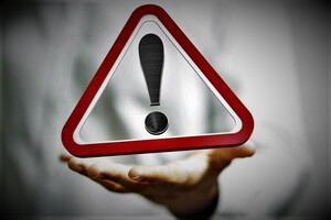 grafika z widocznym wykrzyknikiem wpisanym w trójkąt lewitujący nad dłonią