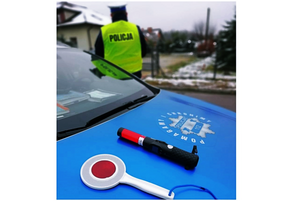 policyjny radiowóz. na masce auta tarcza odblaskowa i promiler. w tle policjant ruchu drogowego w kamizelce odblaskowej z napisem na plecach POLICJA