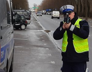 policjant w mundurze i białej czapce ruchu drogowego stojąc przy ulicy mierzy z miernika prędkości