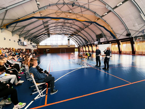 policjanci z wydziału ruchu drogowego na hali sali gimnastycznej prowadzą prelekcję mówiąc przez mikrofon dla blisko 150 osobowej grupy uczniów