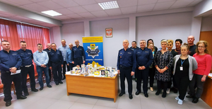 zdjęcie kadry kierowniczej, policjantów i pracowników Komendy Powiatowej Policji w Tomaszowie Mazowieckim przy stole z kartakmi świątecznymi otrzymanymi od partnerów i mieszkańców powiatu tomaszowskiego