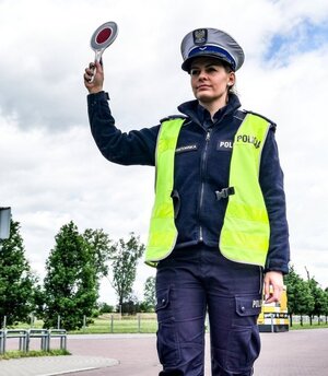 policjantka ruchu drogowego ma podniesioną rękę a w niej tarcze do zatrzymywania pojazdów