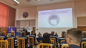 sala konferencyjna , ekran wyświetlający prezentacje dotyczącą Krajowej mapy zagrożeń bezpieczeństwa i prelegenta. większość osób jest w policyjnych mundurach