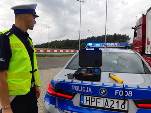 policjant obok radiowozu, a masce leży urządzenie do pomiaru stężenia alkoholu w organizmie