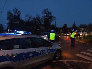 oznakowany radiowóz i umundurowani policjanci pod cmentarzem, po zmroku