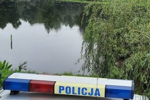 sygnalizator świetlny i dźwiękowy na dachu policyjnego radiowozu. W tle zbiornik wodny. po prawej stronie widoczna korona drzewa