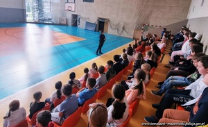 umundurowana policjantka prowadzi profilaktyczną pogadankę z grupa dzieci i młodzieży