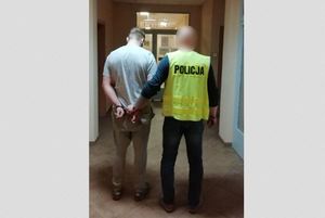 policjant w kamizelce odblaskowej prowadzi korytarzem  komendy mężczyznę w nałożonych na nadgarstki kajdankach