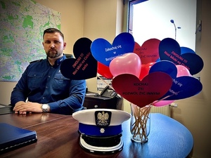 policjant siedzi za stołem, na stole leży czapka policjanta w wazonie na patykach są serduszka z napisami